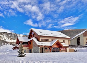 A snow-covered lodge with a wooden facade, a stone entrance, and a mountain backdrop. - CASA-Joubarbe Super 4p terrasse plein sud Arvieux! (Arvieux)