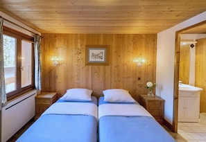 A wooden-paneled room with two beds, a framed picture on the wall, and a bathroom visible through an open door.