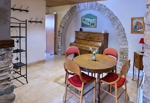 Un espace repas avec une table ronde, des chaises rouges, un piano, des arches en pierre et un porte-manteau fixé au mur.