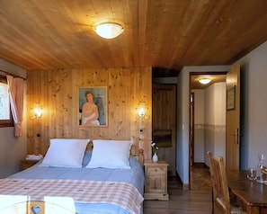 Ein Zimmer mit Holzwänden, einem Bett, Nachttischen, einem Gemälde und einem Essbereich.