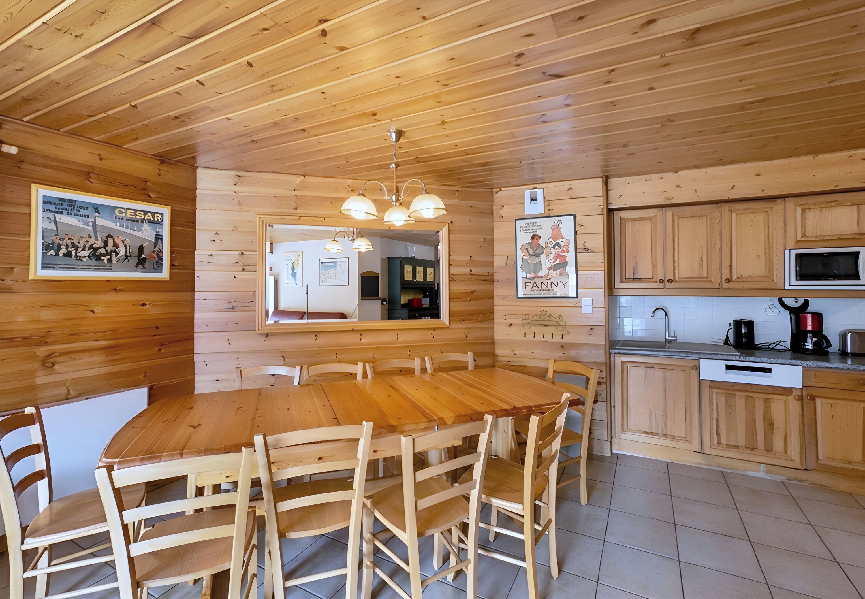 A wooden interior with a round dining table surrounded by chairs, a kitchen area with wooden cabinets, a microwave, and a coffee maker.