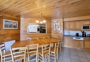 Un intérieur en bois avec une table de salle à manger ronde entourée de chaises, un coin cuisine doté de meubles en bois, d’un four à micro-ondes et d  ’une machine à café.