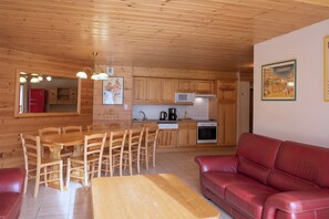 A compact kitchen with wooden cabinets, a dining table with chairs, a red sofa, and a framed picture on the wall.