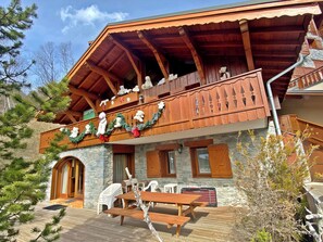 Eine Holzhütte mit einem Balkon, verziert mit Teddybären und Girlanden, Steinmauern und einer Holzterrasse mit Plastikstühlen.