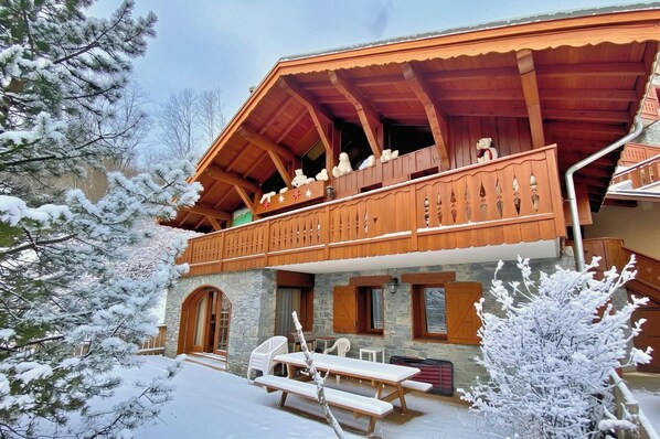 A wooden chalet with a balcony, stone walls, and a snow-covered landscape.