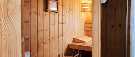 Un sauna en bois avec un banc en bois, un seau en bois et une horloge au mur.
