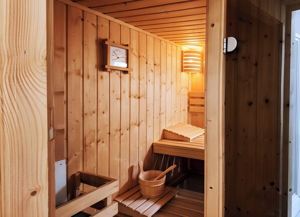 A wooden sauna with a wooden bench, a wooden bucket, and a clock on the wall.