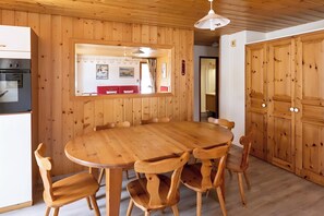 A wooden-paneled room with a round wooden table and chairs, a white ceiling light, and wooden cabinets.