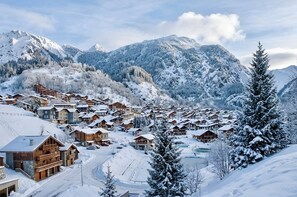 A snow-covered mountain village with wooden chalets, a winding road, and a lake.