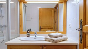 Un baño con tocador de madera, lavamanos, espejo y ducha.