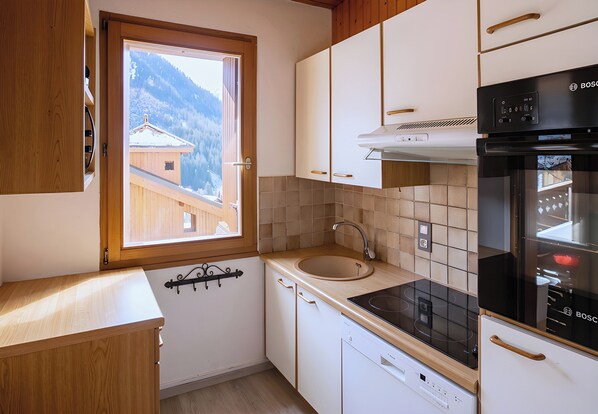 Una cocina con ventana, armarios de madera, un lavamanos y un horno Bosch.