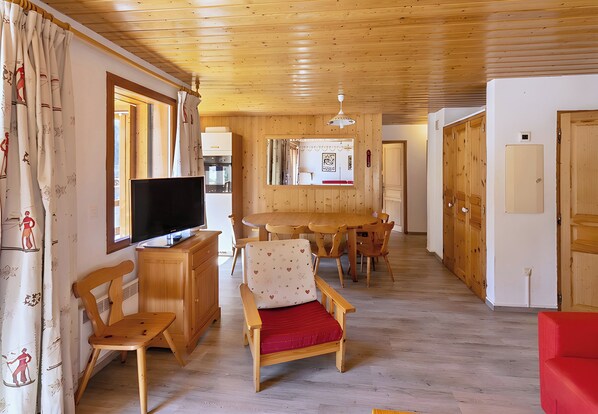 A wooden-paneled room with a television, wooden chairs, a dining table, and a red sofa. - Casa-Le Chargalon N° 11 (Champagny-en-Vanoise)