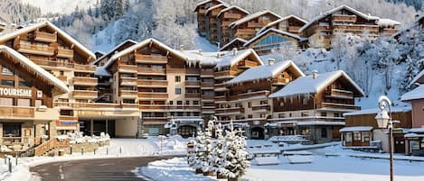 A snow-covered lodge with multiple balconies and a ski slope in the background.