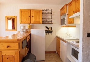 A compact kitchen with wooden cabinets, a coffee maker, a microwave, and a small refrigerator.
