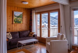 Una habitación acogedora con techo de madera, un cuadro de un paisaje, un sofá, una silla y una mesa.