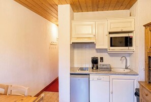 Une cuisine compacte avec des meubles blancs, un four à micro-ondes, une machine à café et un lave-vaisselle.