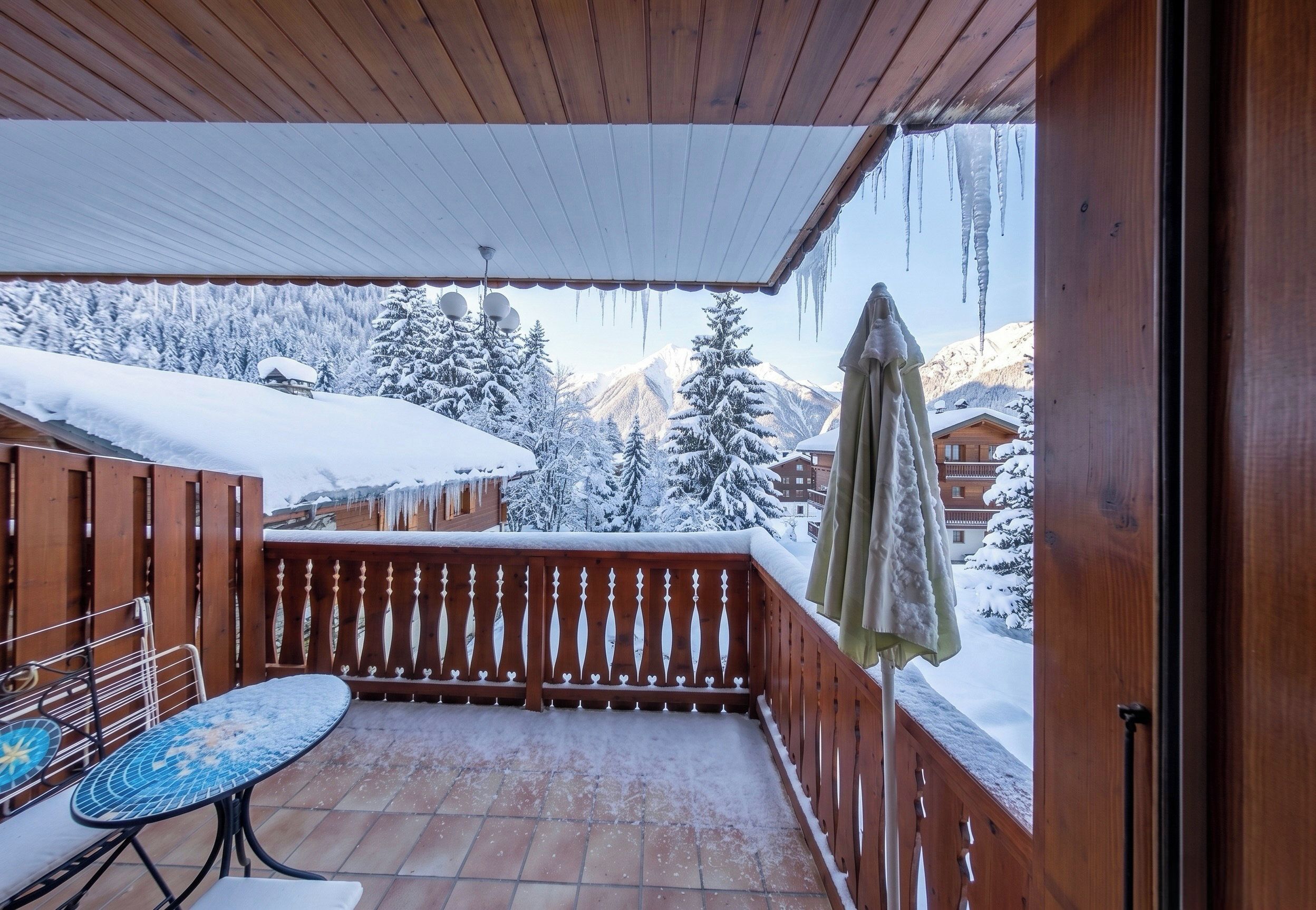 A wooden balcony with a tiled floor, a table, and chairs.