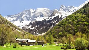 Eine Berglandschaft mit einem Tal, einem kleinen Gebäude mit Schrägdach und blauem Himmel.