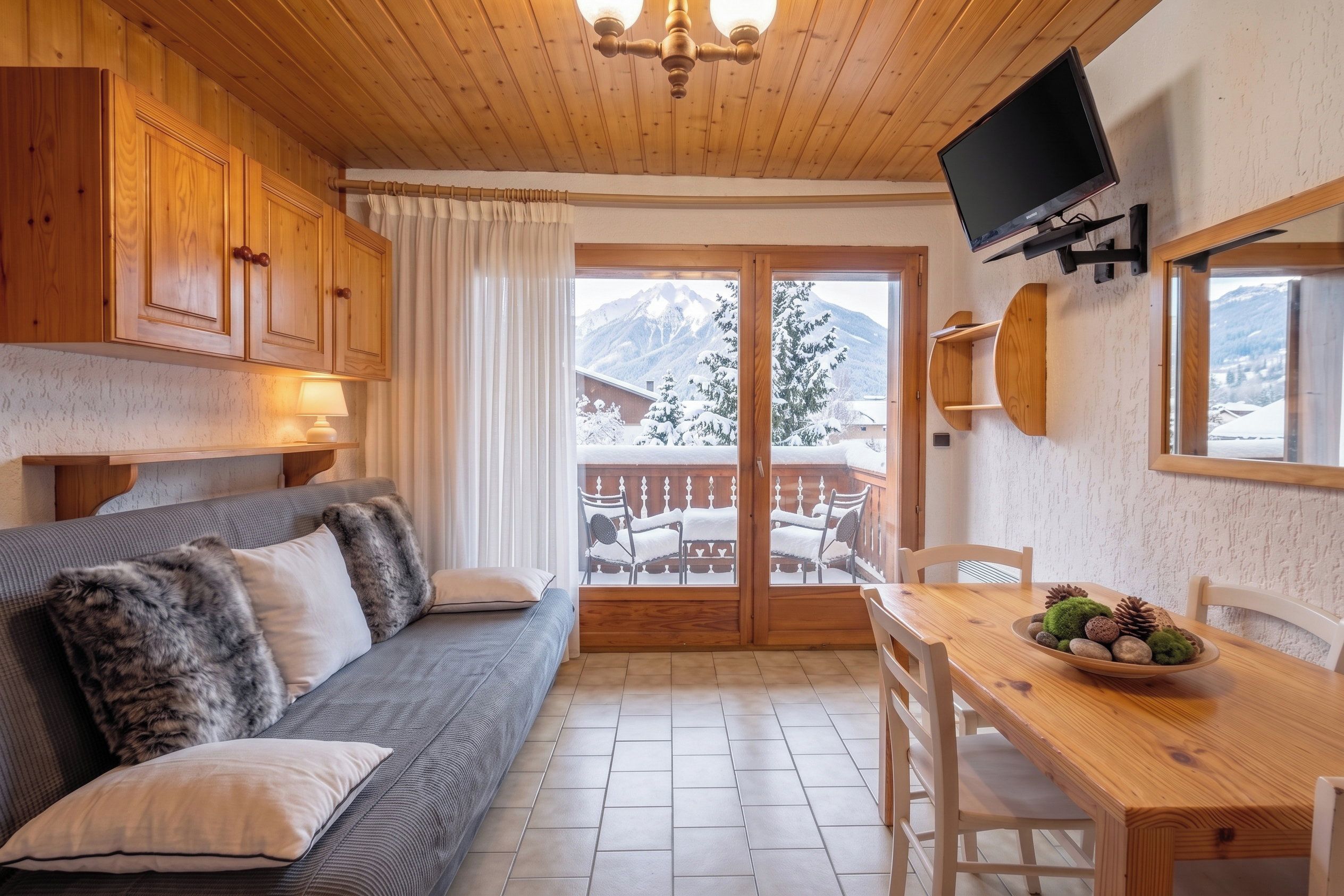 A cozy room with a sofa, a dining table, and a TV mounted on the wall.
