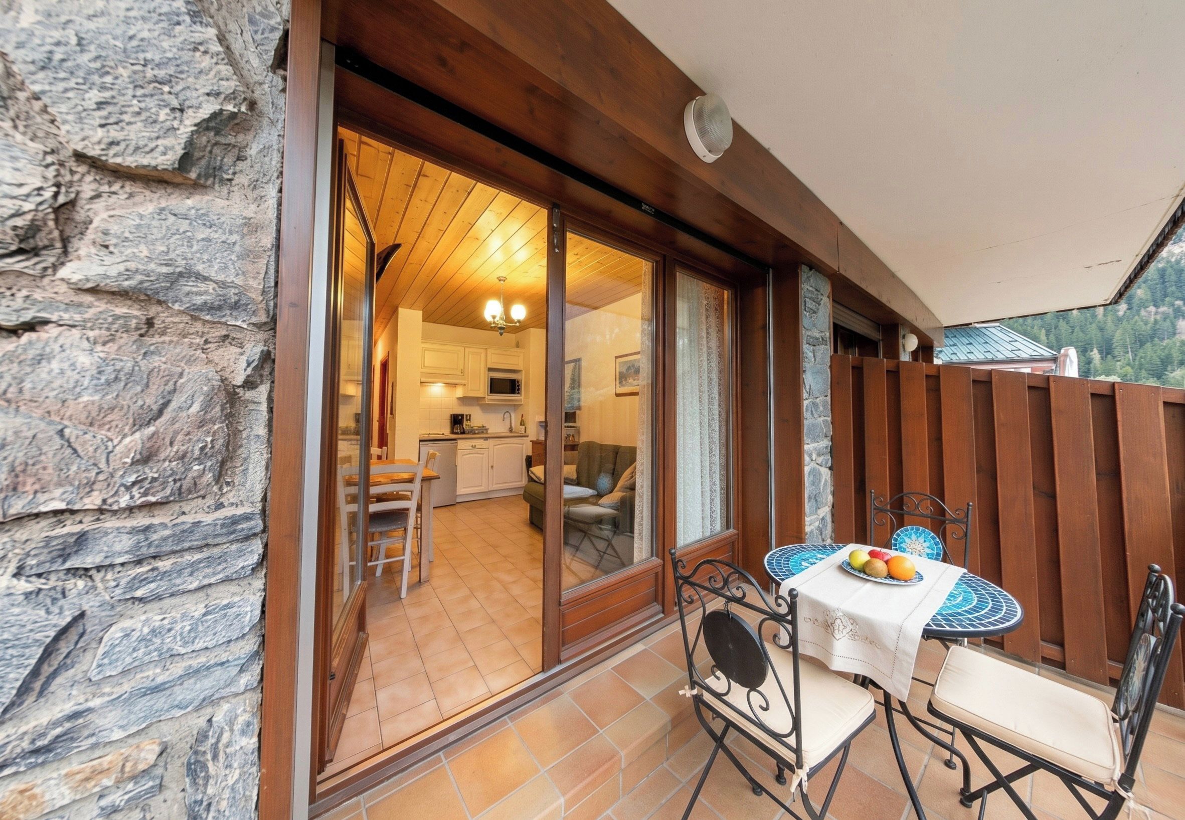 Une terrasse avec une table et des chaises, un mur en pierre et une vue sur une partie de la cuisine.