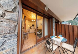 Une terrasse avec une table et des chaises, un mur en pierre et une vue sur une partie de la cuisine.