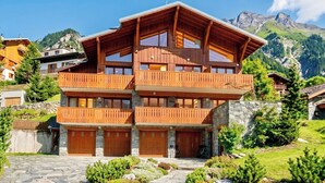Un chalet en bois à plusieurs étages, doté de balcons, de murs en pierre et surplombant un paysage montagneux.