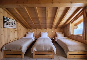 Une pièce avec trois lits en bois alignés contre le mur, un tableau encadré sur la gauche et une fenêtre sur la droite.