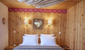 A wooden-paneled room with a bed, two wall-mounted lamps, a heart-shaped mirror, and a small clock on the nightstand.