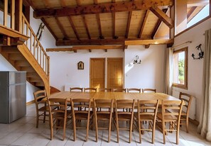 A dining area with a wooden table and chairs, a staircase, and a view of the outdoors through a window. - CASA-Chalet du Merle 2 à Champagny-en-Vanoise (Champagny-en-Vanoise)
