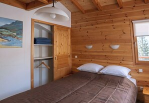 A bedroom with a bed, a wardrobe, a painting, and a window.