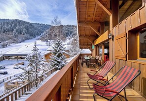 A wooden balcony with a view of a snowy landscape and a ski lift.