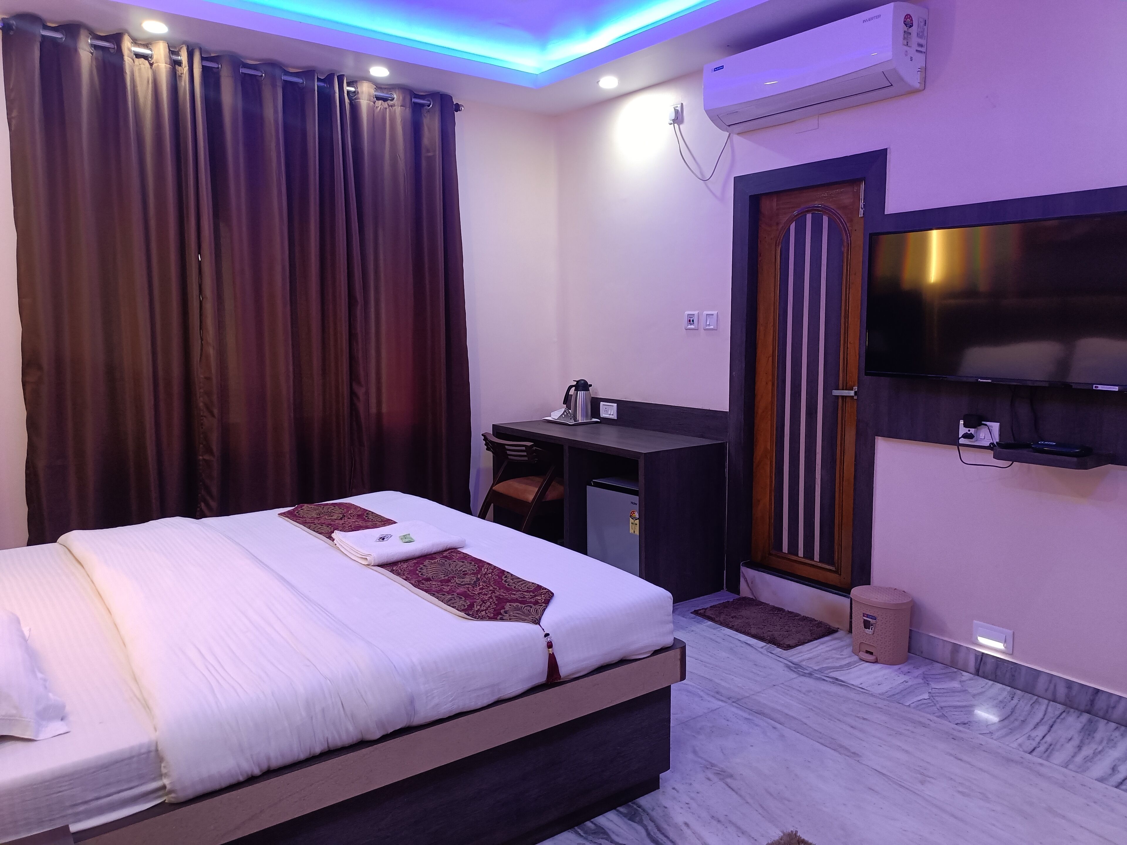 Habitación de hotel con cama, escritorio, silla, televisor, equipo de aire acondicionado y un pequeño cubo de basura.