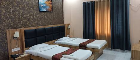 A hotel room with two beds, a wooden headboard, a bedside table with a lamp, a wall-mounted air conditioner, and a painting of a beach scene.