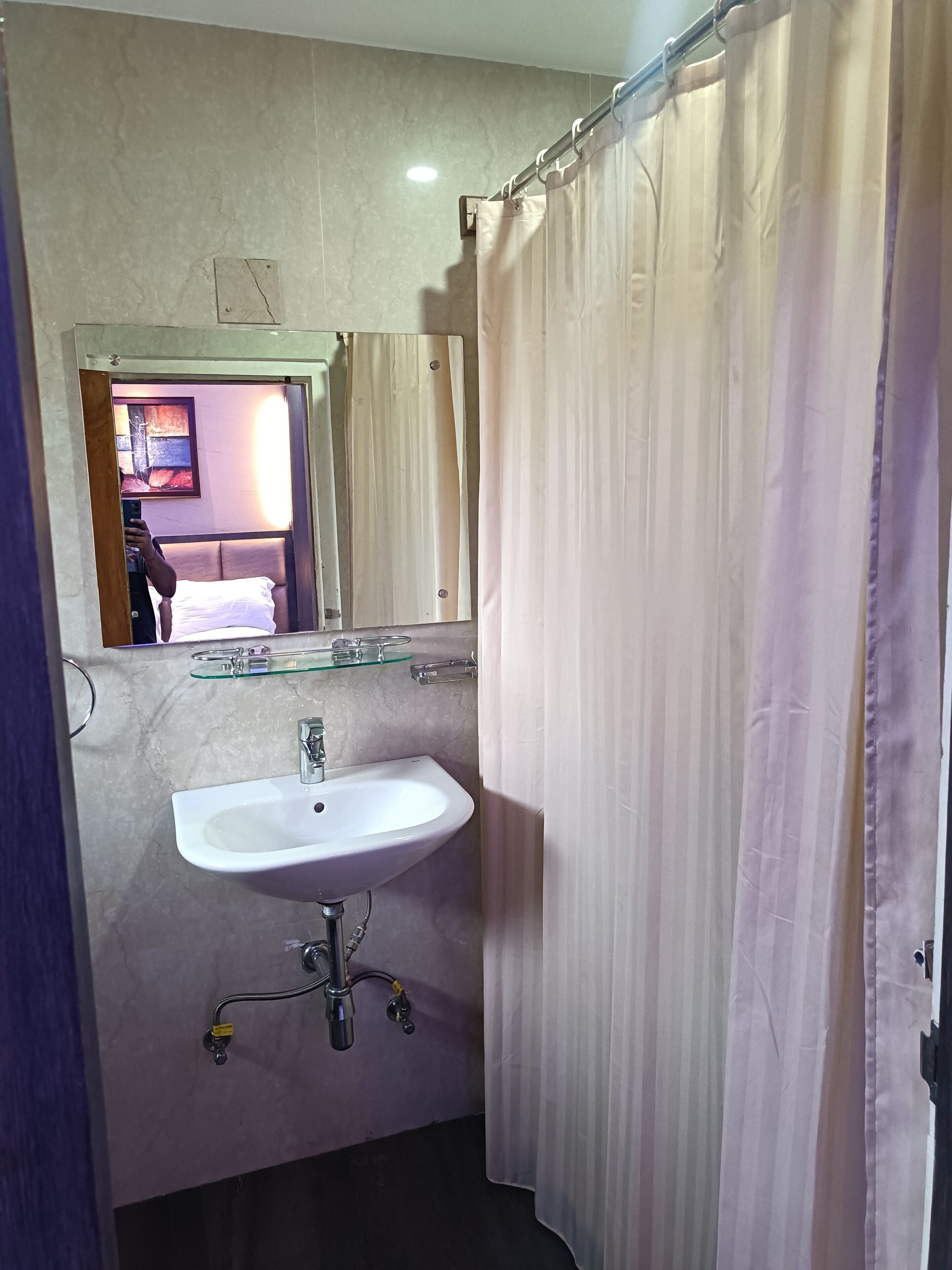 Un baño con un lavabo blanco, un estante de vidrio encima y una cortina de ducha.
