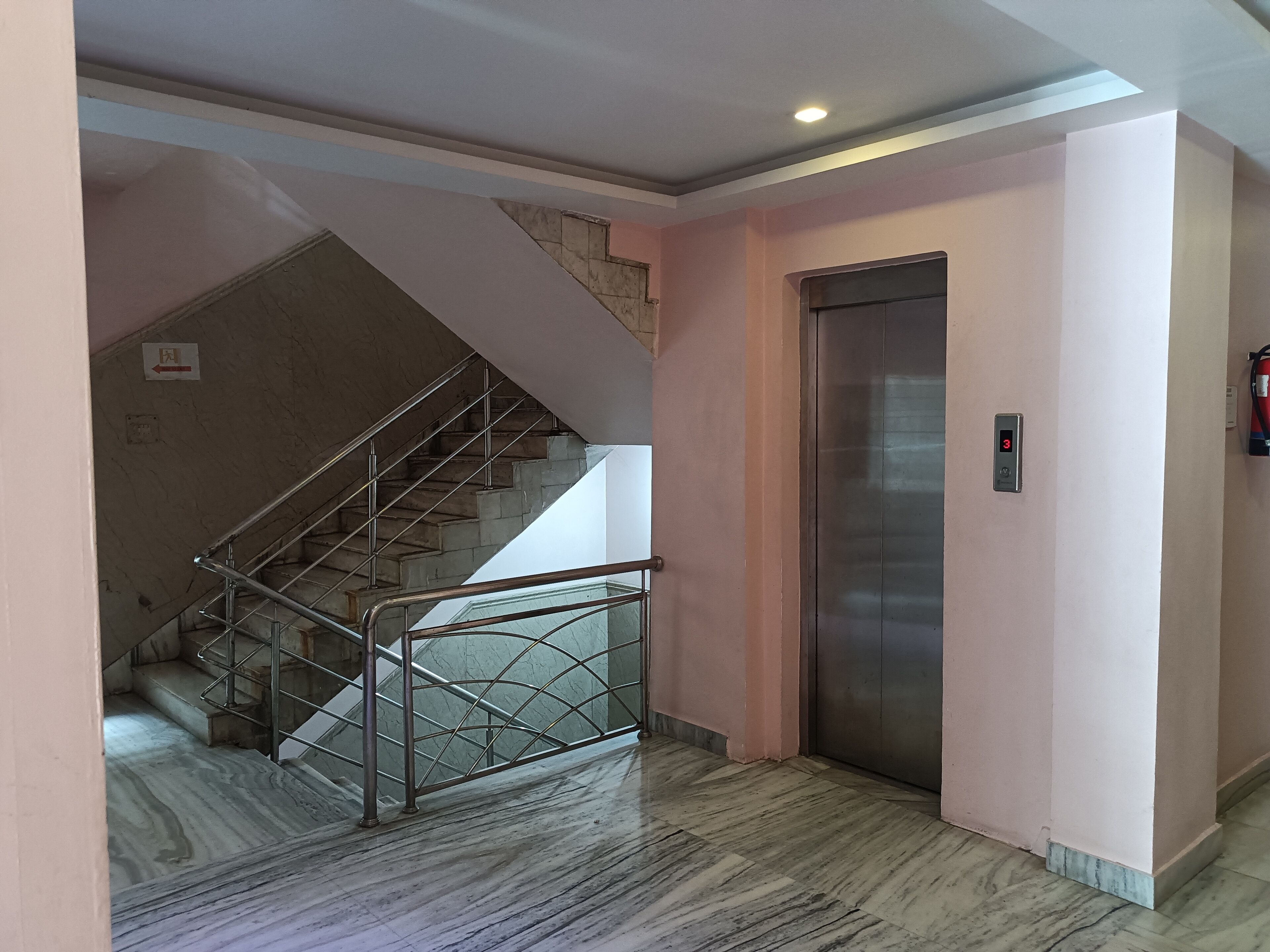 A marble-floored hallway with a staircase, an elevator, and a fire extinguisher.