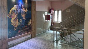 Una escalera de mármol con barandillas de metal, un mural con la imagen de una figura tocando una flauta, y una ventana con cristales de celosía.
