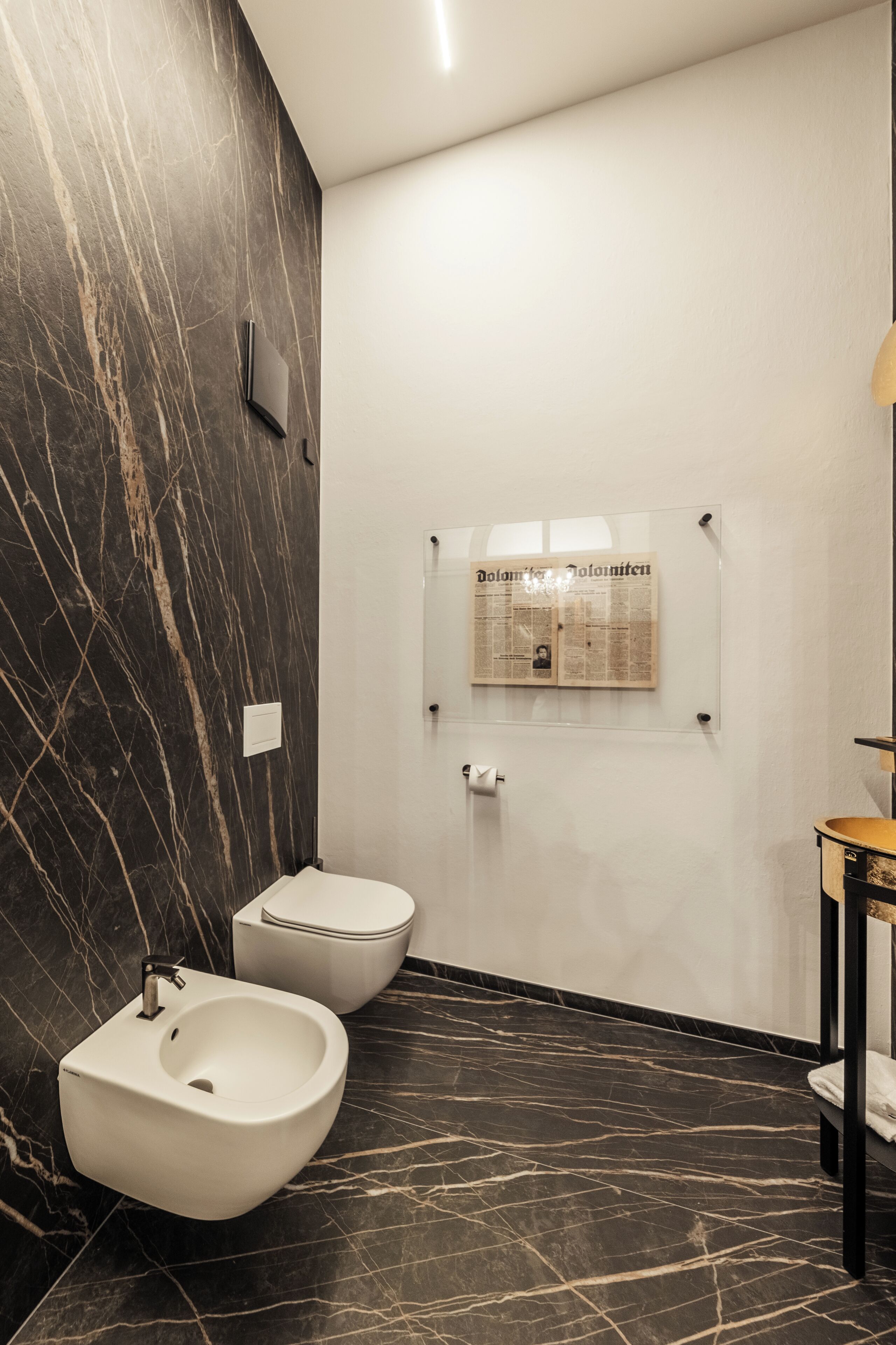 Un baño moderno con bidé, inodoro y un periódico en la pared.