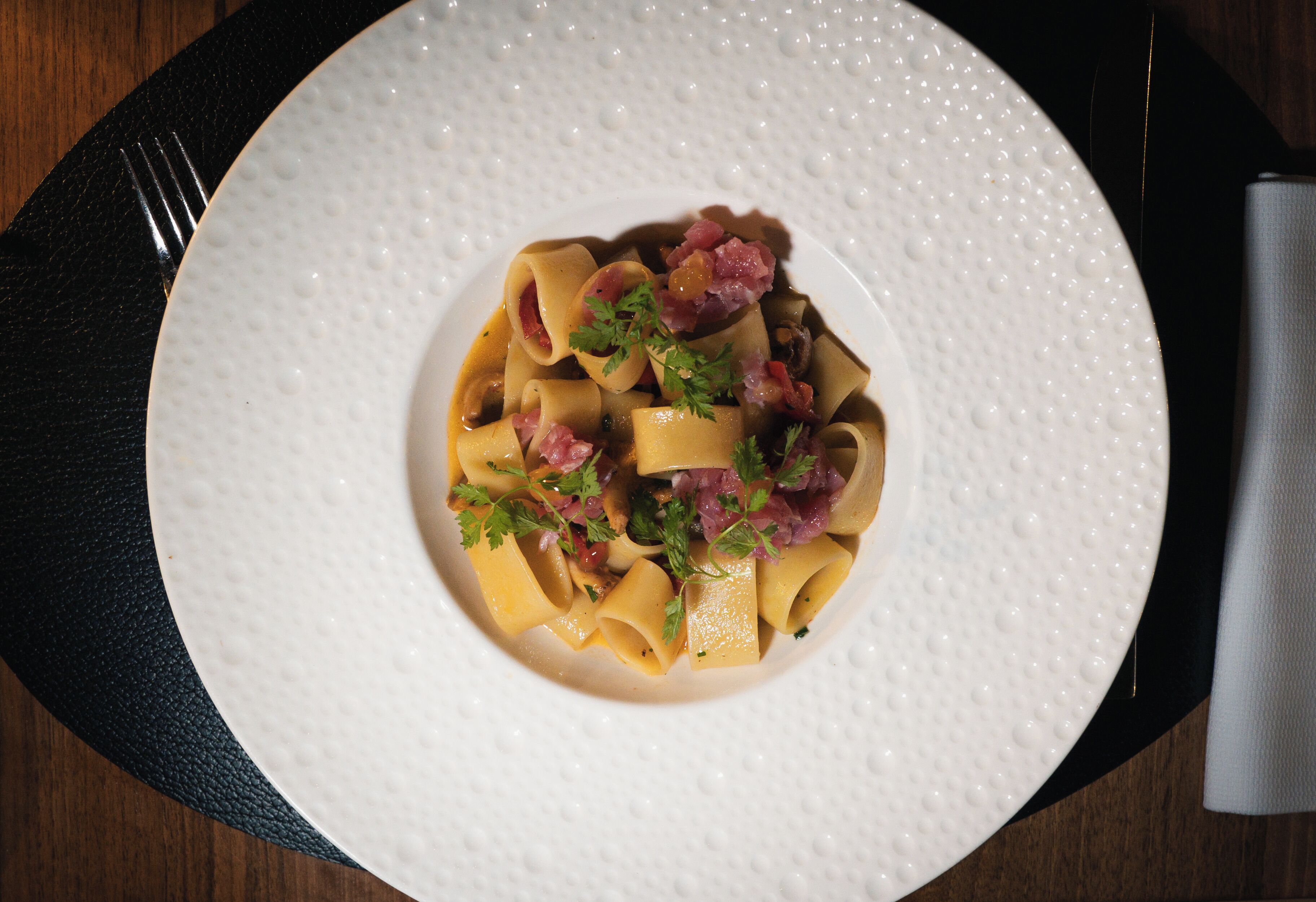 A white plate with pasta and garnishes on a dark table.
