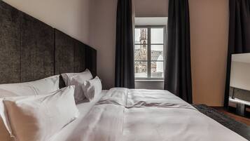 A neatly made bed with white linens and pillows, a dark headboard, and a window with a view of a building.