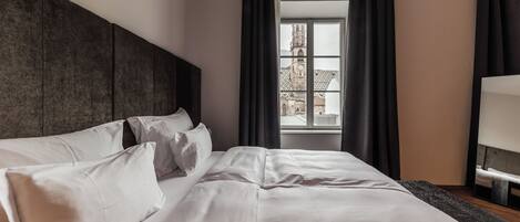 Ein ordentlich bezogenes Bett mit weißen Leinen und Kissen, ein dunkles Kopfteil und ein Fenster mit Blick auf ein Gebäude.