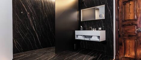 A modern bathroom with a wooden vanity, marble walls, and a wooden door.