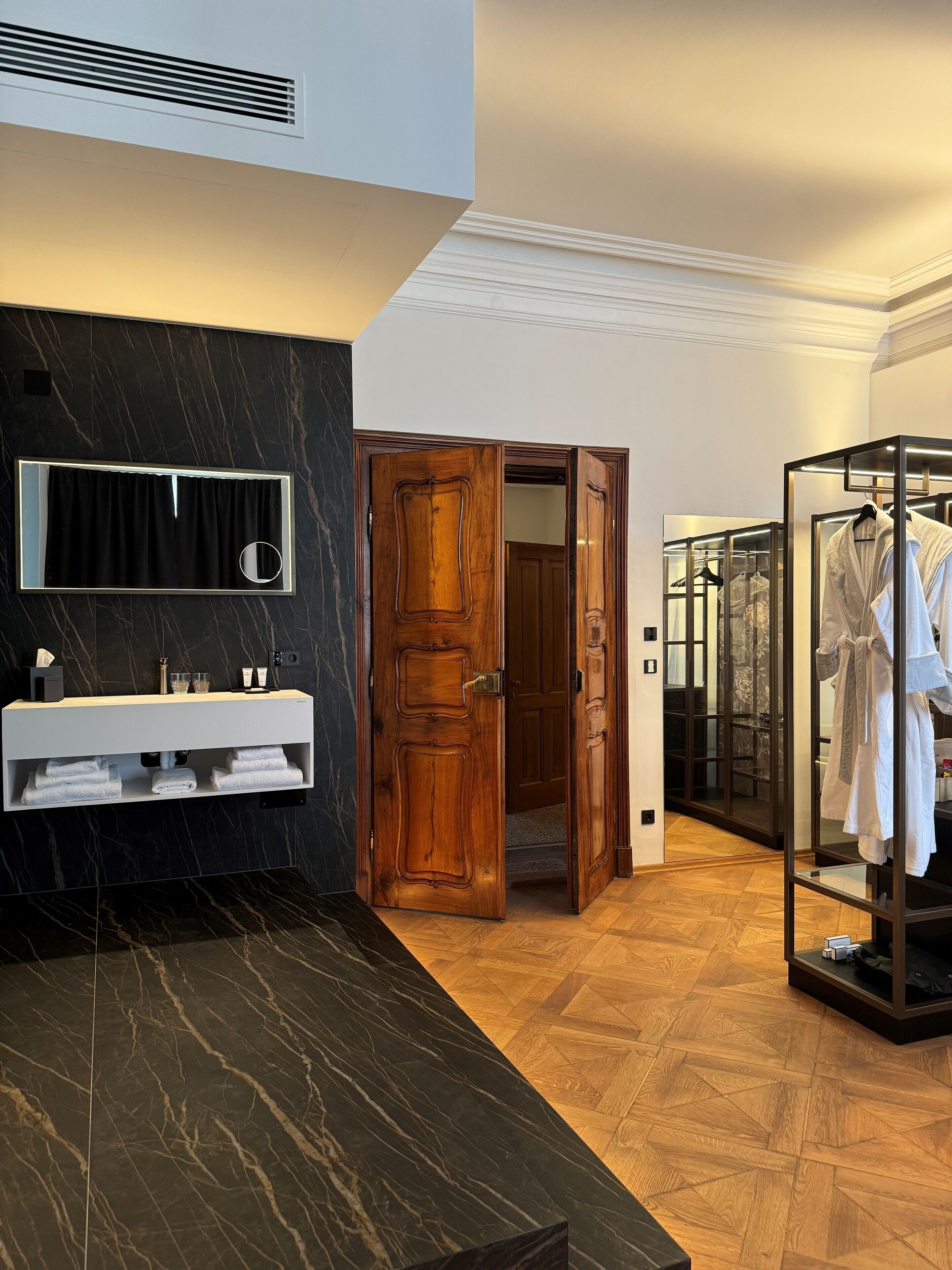 Een moderne badkamer met een marmeren wastafelmeubel, een houten deur en een inloopkast met een glazen deur.