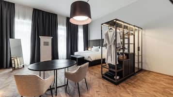 Habitación de hotel moderna con cama, una mesa redonda, dos sillas, armario para batas y un espejo grande.