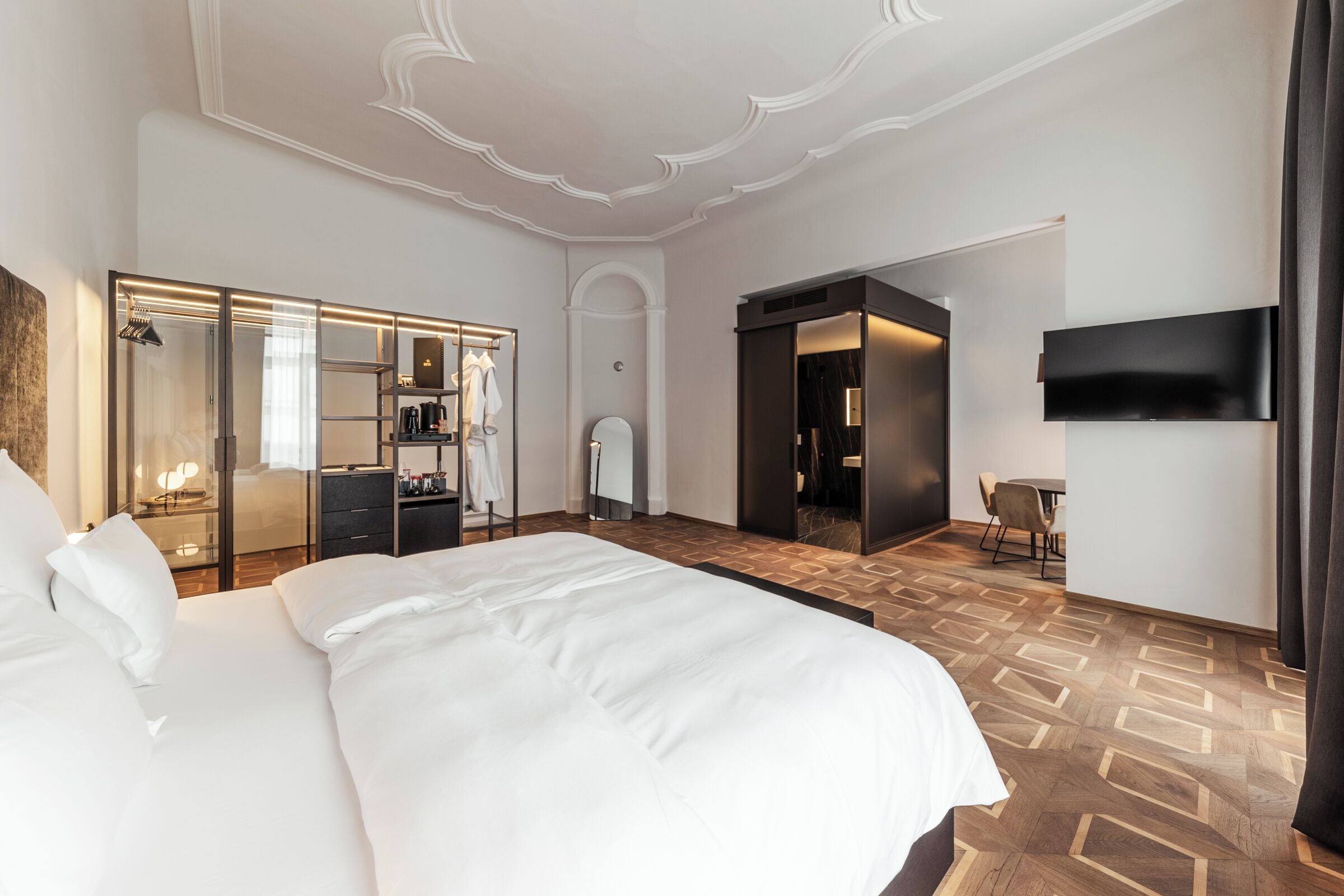 A hotel room with a large bed, a walk-in closet, a bathroom, and a TV mounted on the wall.