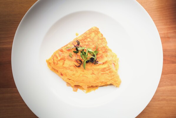 A white plate with a slice of omelette garnished with microgreens. - META SUITES historic city living (Bolzano)