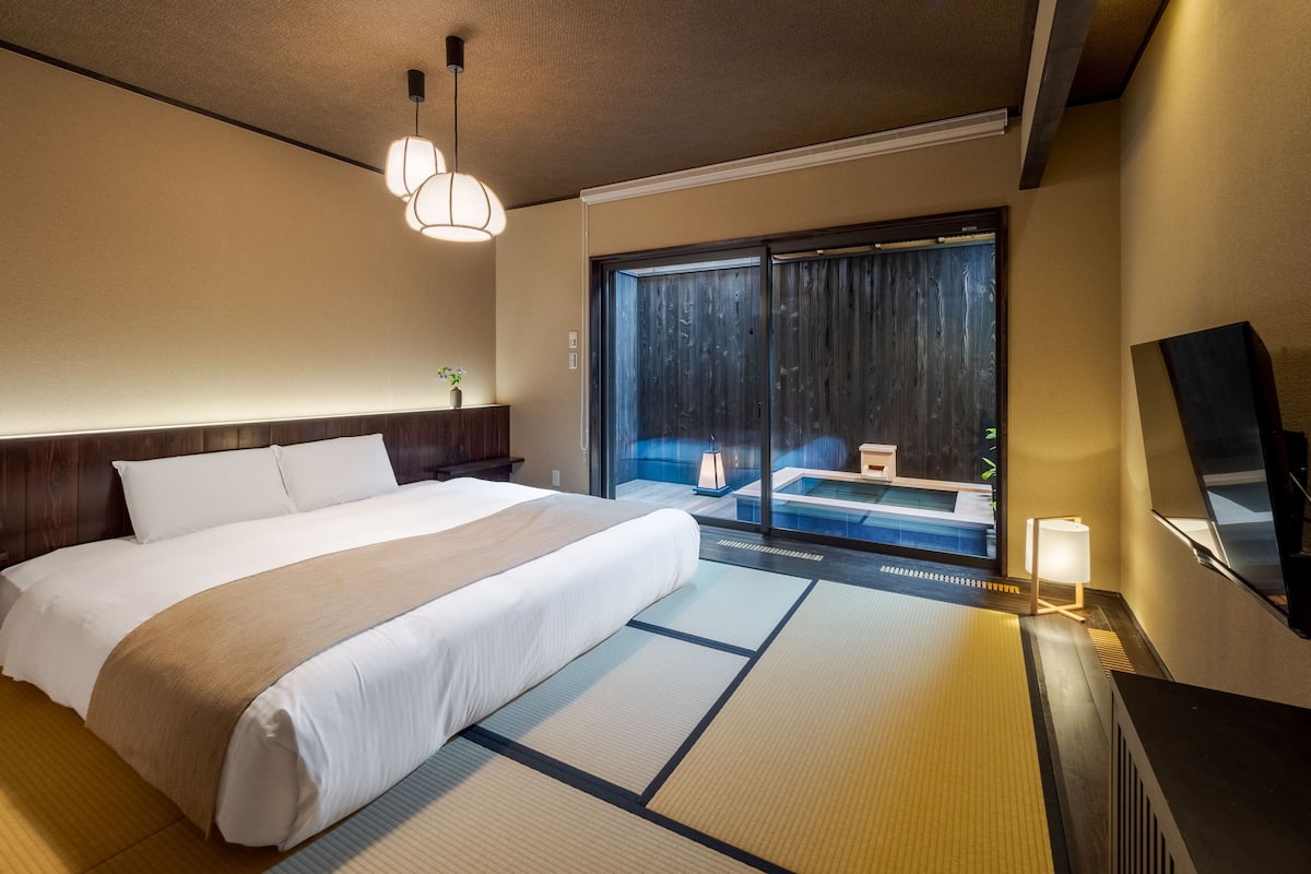 Ein Hotelzimmer mit einem großen Bett, einer Schiebetür zum Balkon, einem Nachttisch mit Lampe und einem an der Wand befestigten Fernseher.