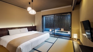 A hotel room with a large bed, a sliding glass door leading to a balcony, a small table with a lamp, and a TV on a stand. - ROJIYU KYOTO (Kyoto)