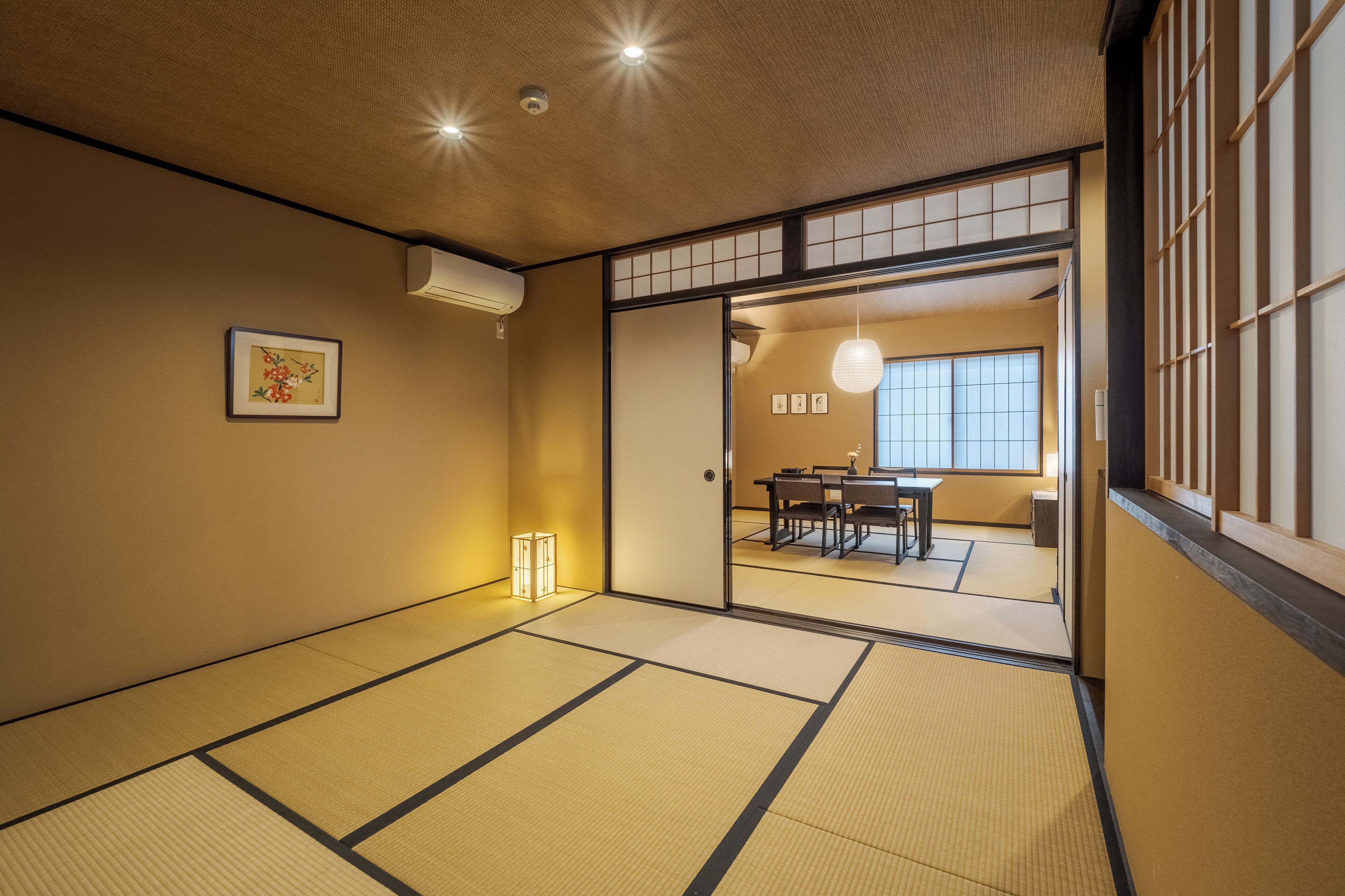 A traditional Japanese room with tatami flooring, a sliding door leading to a dining area, and a hanging lantern.