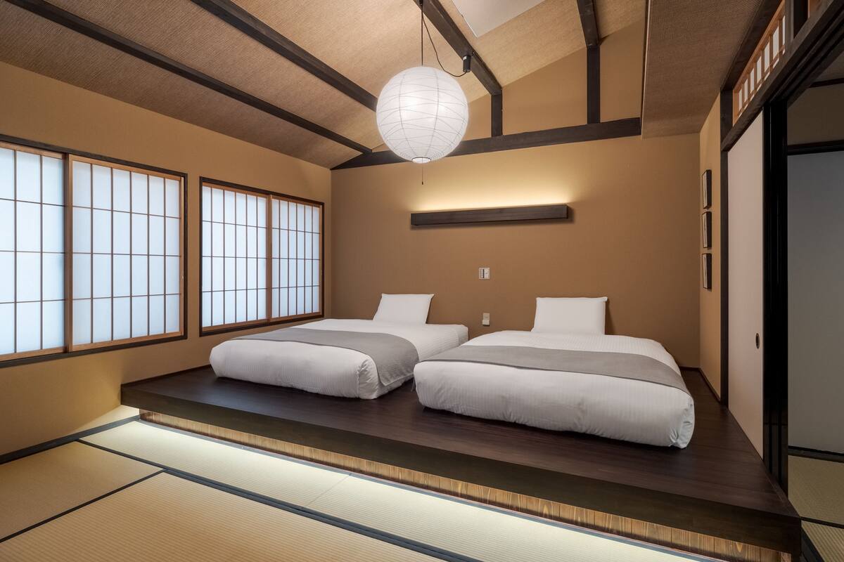 Ein traditioneller japanischer Raum mit Tatami-Boden, zwei Betten, einem Shoji-Bildschirm und einer hängenden Papierlaterne.