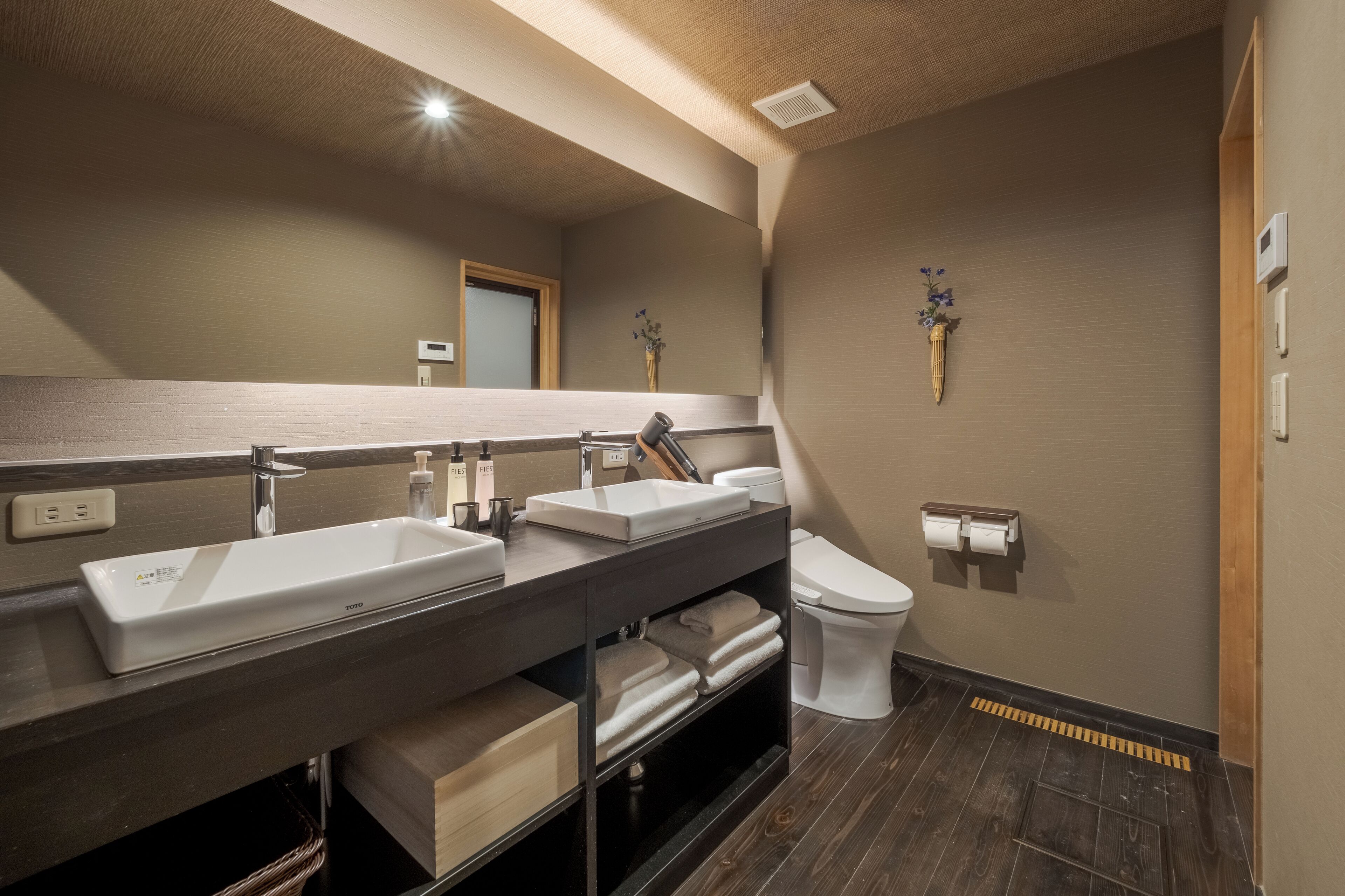 Un baño moderno con un espejo grande, dos lavamanos, un inodoro y un perchero para toallas.
